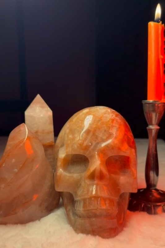 A Fire Quartz Crystal Flame, Tower, Skull Set on a Soft and Furry White Blanket with a Lit Orange Candle next to it