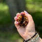 Cut base dark raw citrine crystal cluster displayed in hand with gemstone bracelets in natural sunlight