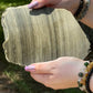 Close-up of a polished Golden Obsidian slab with visible golden shimmer and raw edges, displayed in natural sunlight.