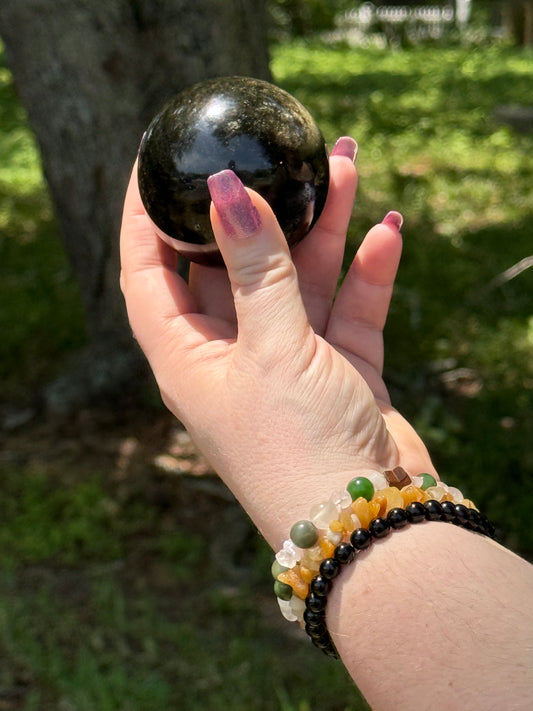Golden Obsidian sphere held in hand outdoors, showcasing its polished surface with subtle golden sheen—used for grounding, protection, and energy work.