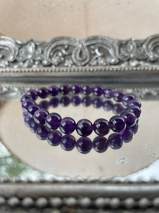 Handmade Amethyst bracelet featuring polished purple gemstone beads displayed on a mirrored silver tray, ideal for Third Eye and Crown Chakra healing