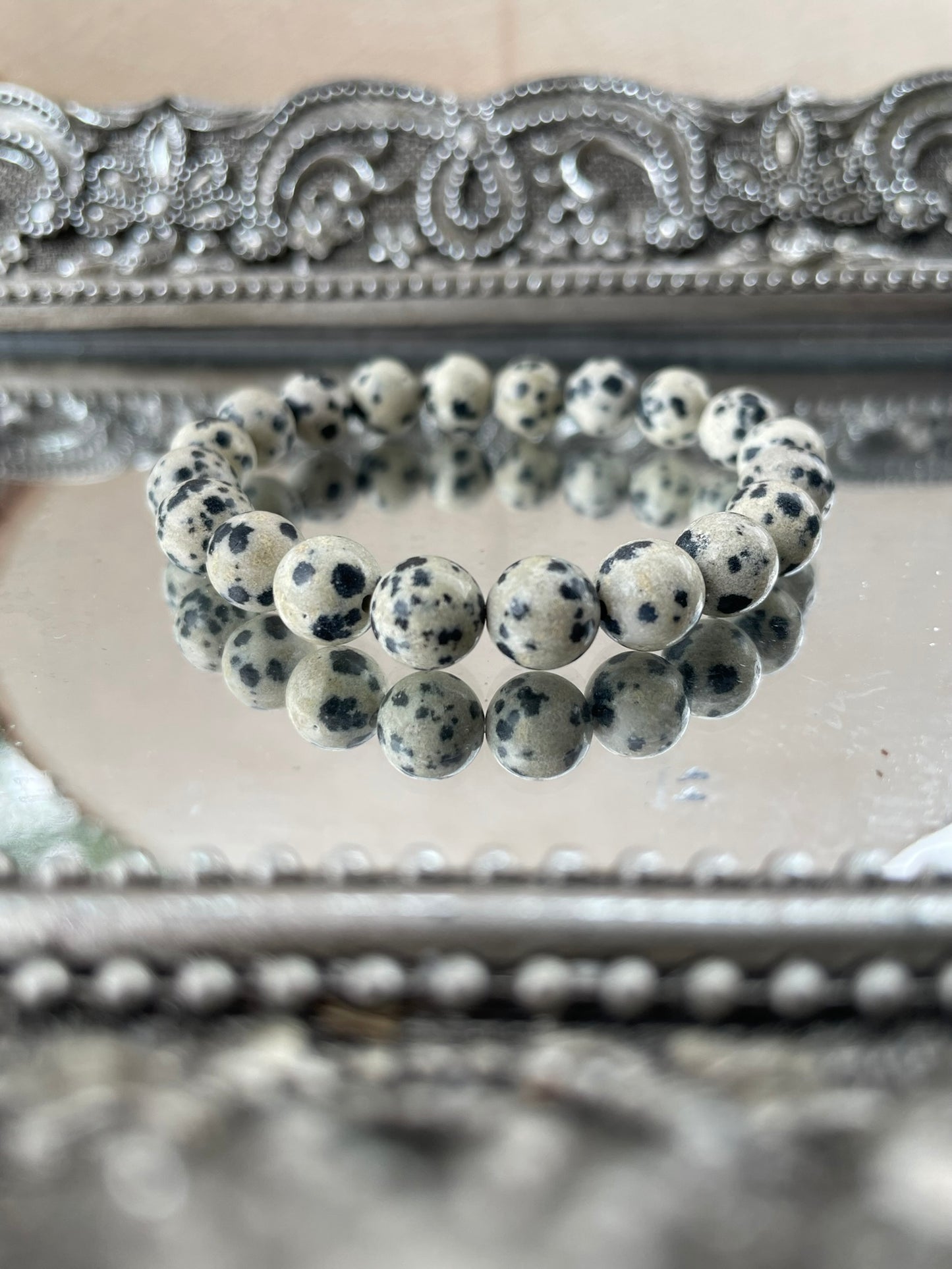 Handmade Dalmatian Jasper bracelet featuring natural spotted beads displayed on a mirrored silver tray, symbolizing grounding and joyful energy for chakra healing