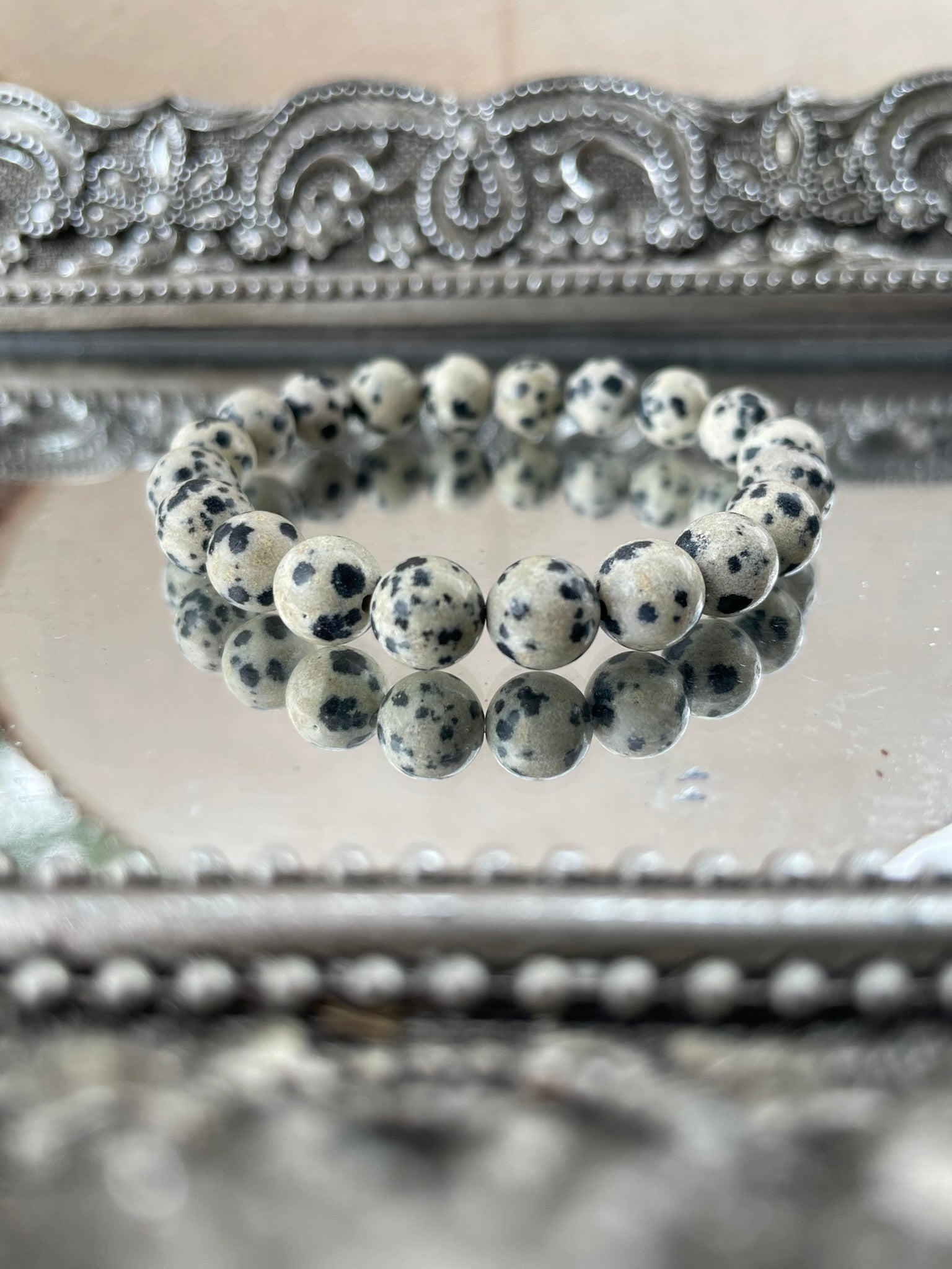 Handmade Dalmatian Jasper bracelet featuring natural spotted beads displayed on a mirrored silver tray, symbolizing grounding and joyful energy for chakra healing