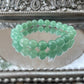 Handmade Green Aventurine bracelet displayed on a mirrored surface, featuring polished green beads for heart chakra healing, luck, and prosperity attraction