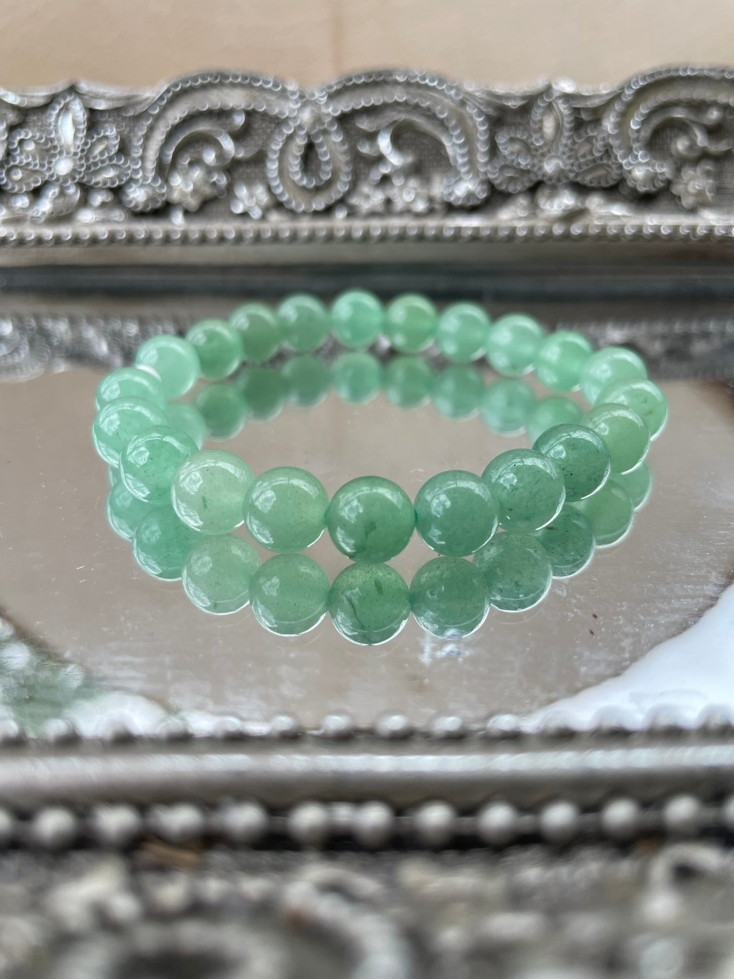 Handmade Green Aventurine bracelet displayed on a mirrored surface, featuring polished green beads for heart chakra healing, luck, and prosperity attraction