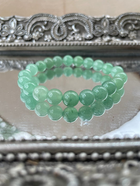 Handmade Green Aventurine bracelet displayed on a mirrored surface, featuring polished green beads for heart chakra healing, luck, and prosperity attraction