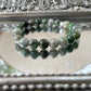 Handmade Green Jade bracelet with polished green beads displayed on a reflective mirrored surface, used for heart chakra healing, luck, and prosperity