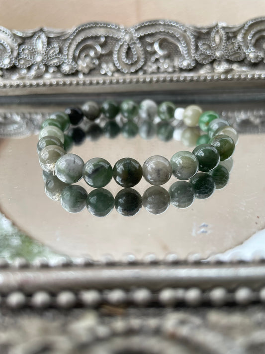 Handmade Green Jade bracelet with polished green beads displayed on a reflective mirrored surface, used for heart chakra healing, luck, and prosperity
