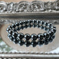Handmade Hematite bracelet with glossy black beads reflecting light, displayed on a mirrored surface for grounding and root chakra healing