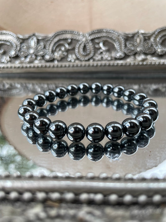 Handmade Hematite bracelet with glossy black beads reflecting light, displayed on a mirrored surface for grounding and root chakra healing