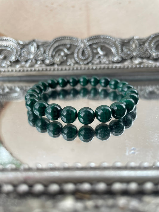 Handmade Malachite bracelet with deep green swirling beads displayed on a reflective silver tray, ideal for Heart Chakra healing and energy protection