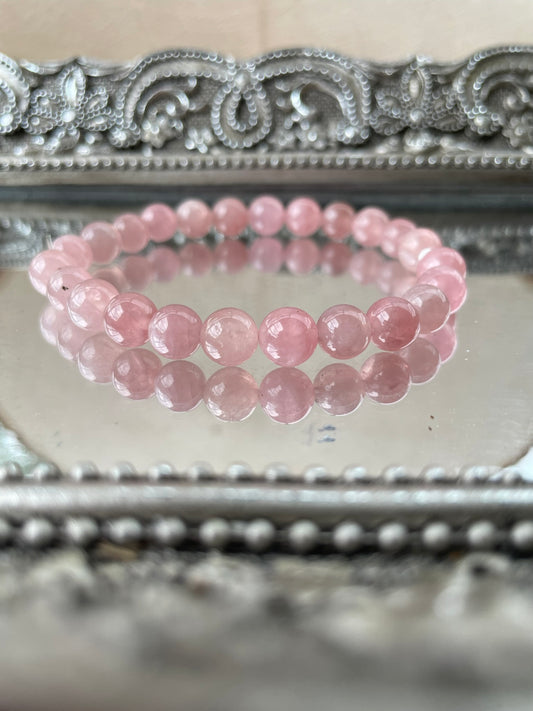 Handmade Rose Quartz bracelet with polished pink crystal beads displayed on an ornate mirrored surface, ideal for heart chakra healing and self-love energy