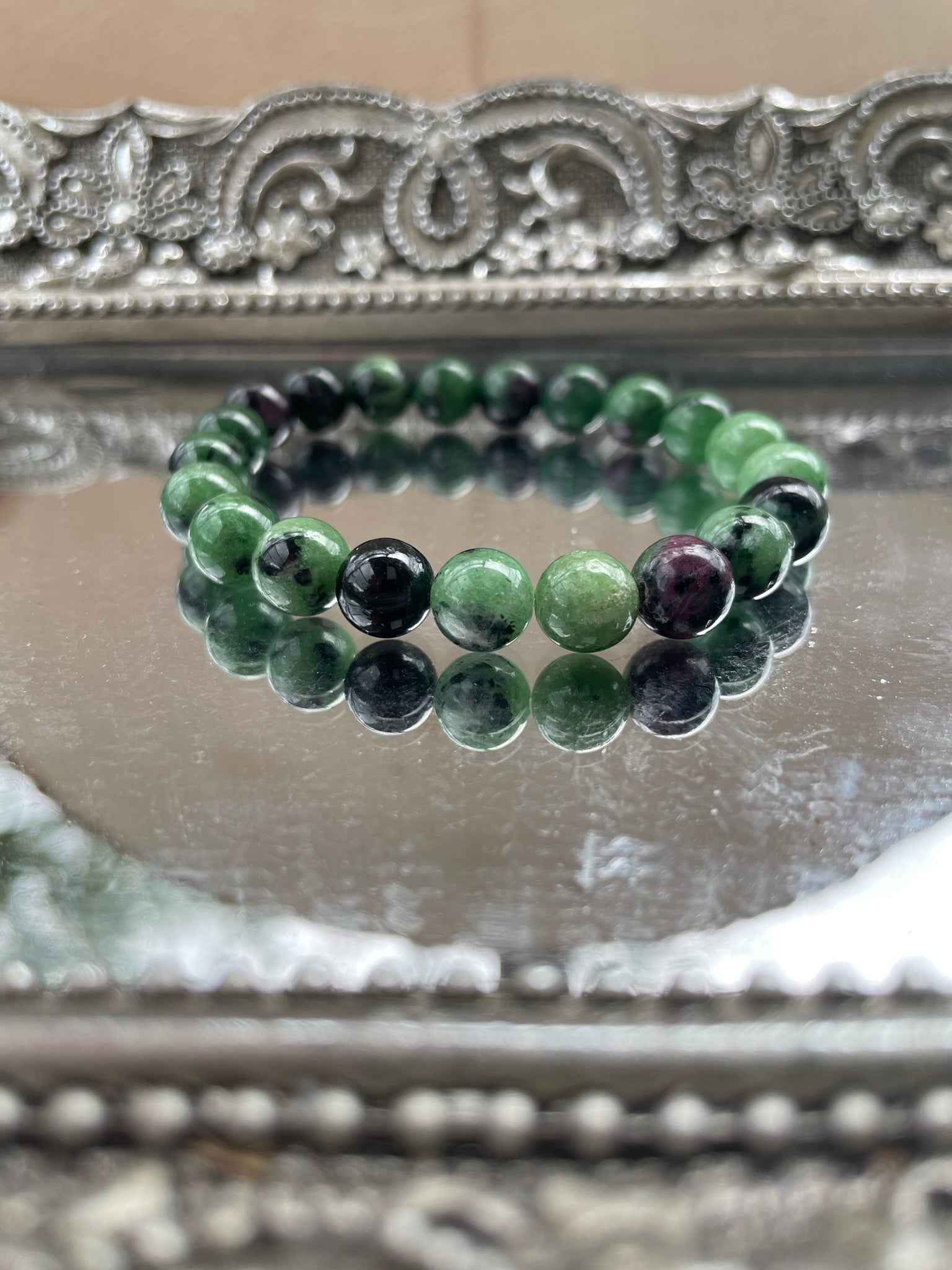 Handmade Ruby in Zoisite bracelet featuring green and deep pink gemstone beads displayed on a silver reflective surface, ideal for heart chakra and emotional healing