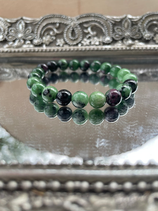 Handmade Ruby in Zoisite bracelet featuring green and deep pink gemstone beads displayed on a silver reflective surface, ideal for heart chakra and emotional healing