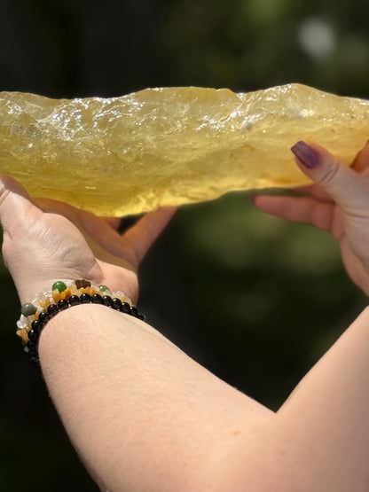 Side profile of a large translucent citrine slab glowing in natural sunlight, emphasizing its elongated free-form shape and deep golden tone.
