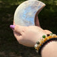 Moonstone crescent moon carving held in hand, displaying a vivid blue flash across its polished surface—used for intuition, feminine energy, and lunar rituals.