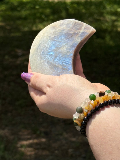 Moonstone crescent moon carving held in hand, displaying a vivid blue flash across its polished surface—used for intuition, feminine energy, and lunar rituals.