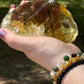 Front view of a natural smoky citrine free-form crystal held in hand, showcasing deep golden tones and translucent clarity under sunlight.