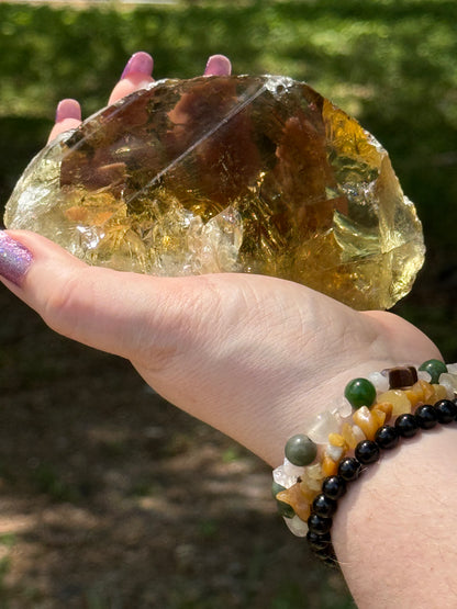 Front view of a natural smoky citrine free-form crystal held in hand, showcasing deep golden tones and translucent clarity under sunlight.