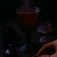 A dark fantasy-inspired photo of spiced white pear tea poured into a black goblet, surrounded by obsidian, amethyst crystals, and a silver ring, with violet light reflecting off the stones—capturing the essence of the Obsidian Heart tea blend.