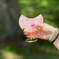 Hand holding a Rose Quartz crescent moon on a gold stand, symbolizing love and heart chakra healing in natural light