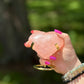 Rose Quartz heart-shaped crystal on gold stand held in hand outdoors, symbolizing love, healing, and Heart Chakra energy
