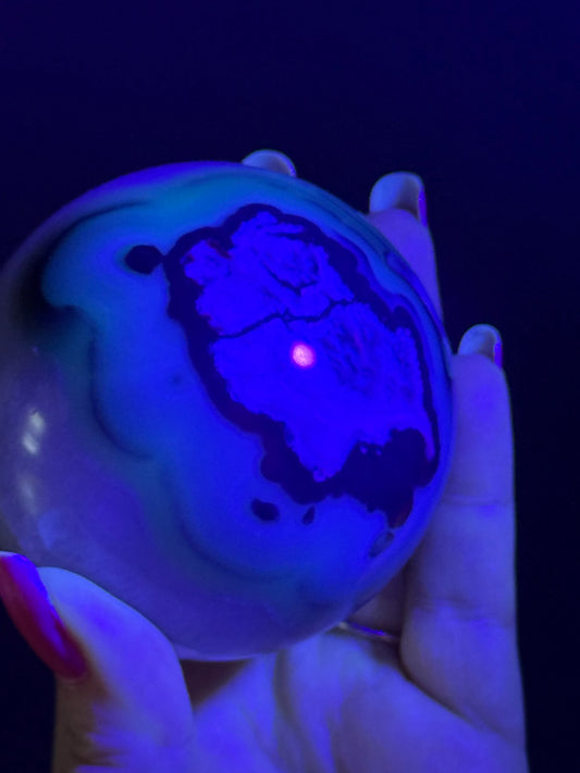 Volcano Agate Sphere glowing under UV light, revealing its fluorescent patterns while being held in hand