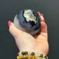 Polished Volcano Agate Sphere showing unique natural patterns and cream inclusions, displayed in a hand with chakra bracelets
