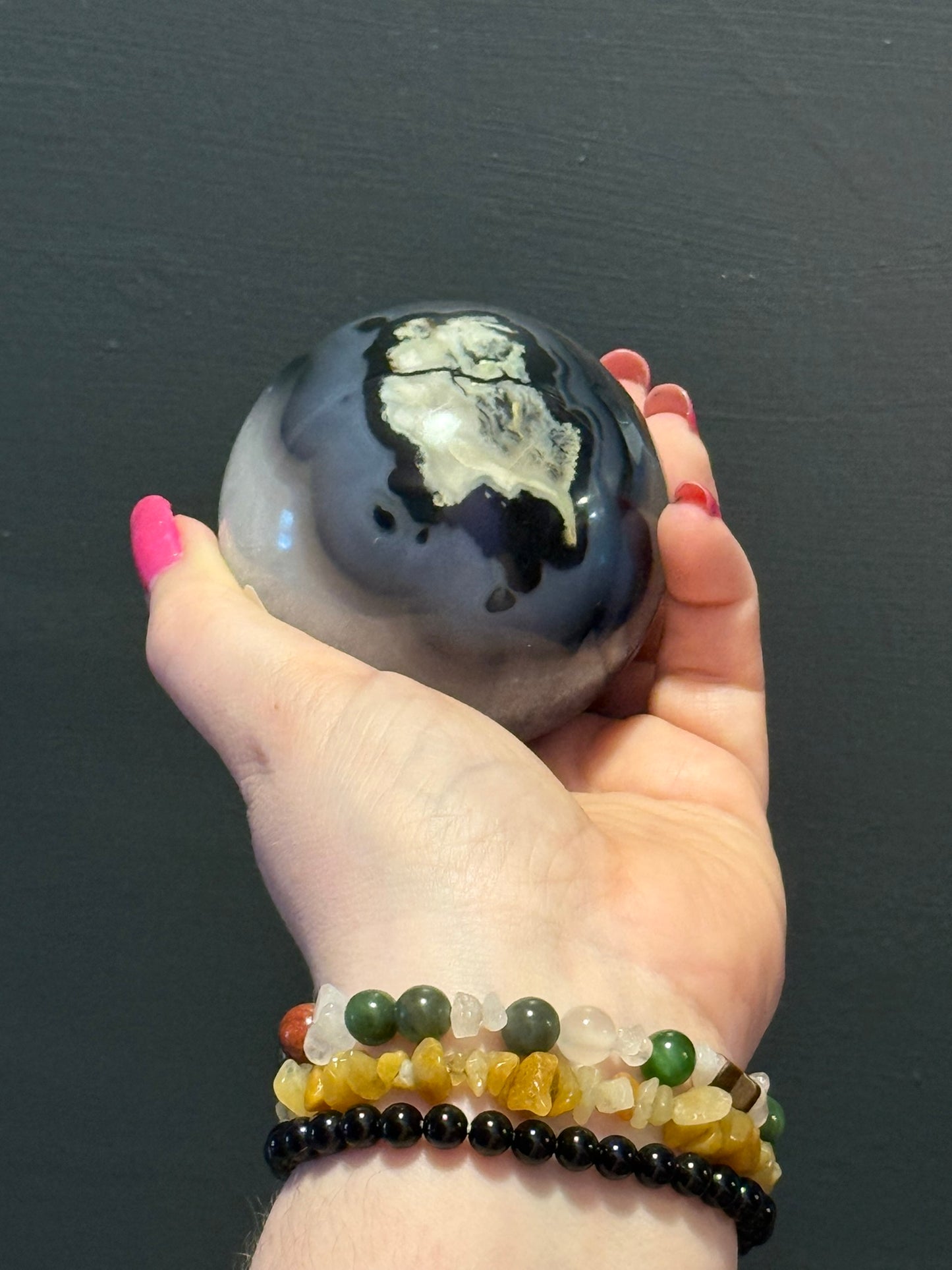 Polished Volcano Agate Sphere showing unique natural patterns and cream inclusions, displayed in a hand with chakra bracelets